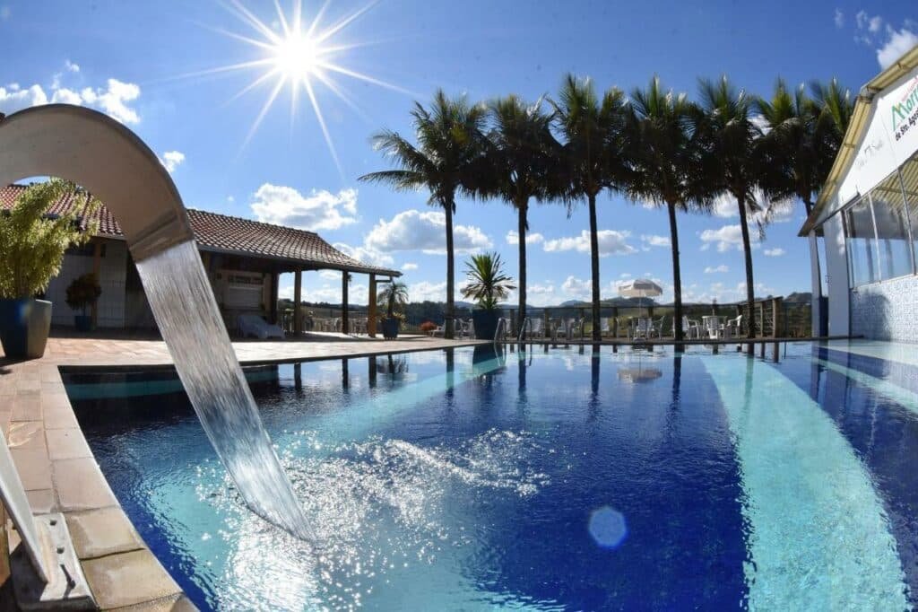 Piscina ampla e com uma pequena cascata no Hotel Morro De Santo Agostinho com palmeiras ao redor do deck