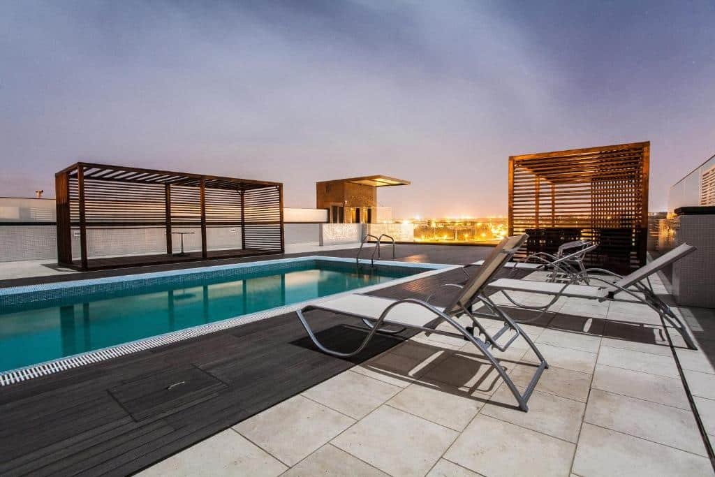 Terraço do Hotel Pérola em Praia que mostra uma grande piscina ao ar livre com algumas espreguiçadeiras em volta e algumas construções de madeira. Imagem ilustrando post Hotéis em Cabo Verde.