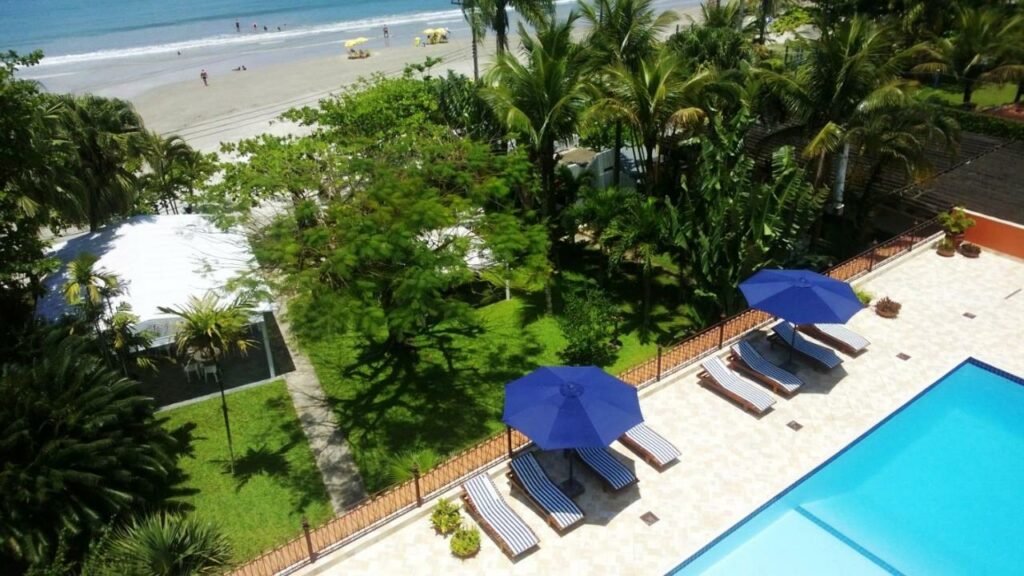 Deck com piscina, espreguiçadeiras, guarda-sóis, piscina e jardins logo antes da Praia da Enseada, em Ubatuba, no Hotel Porto Di Mare. 