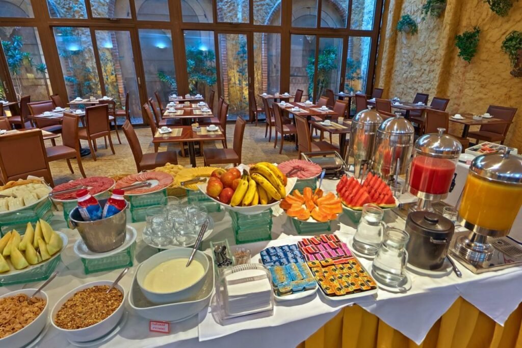Restaurante do Hotel Shelton com cadeiras e mesas de madeira com muitas portas de vidro viradas para o jardim