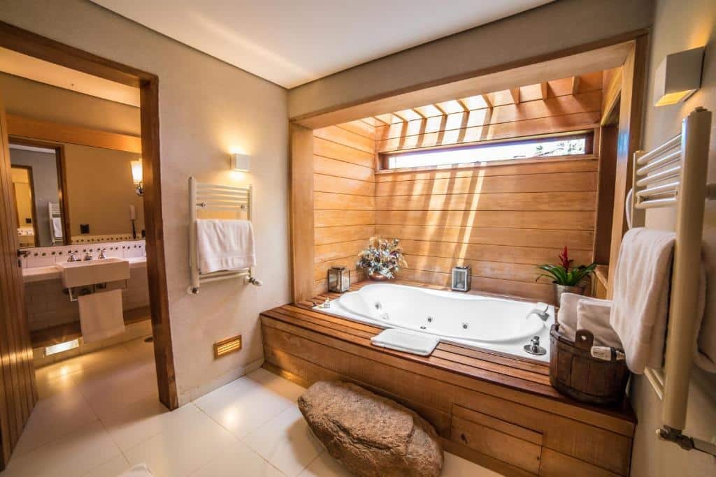 Banheiro amplo do Hotel Toriba com uma banheira de hidromassagem com um pequeno deck ao redor com vasos de flores e toalhas brancas