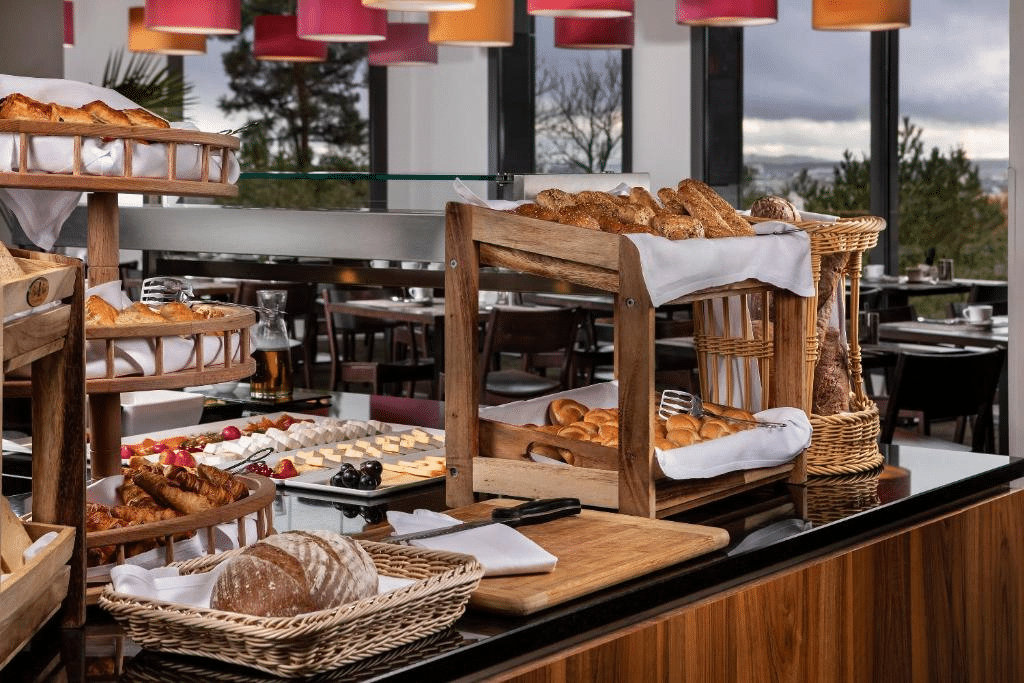 Foto do buffet servido no Melia Luxembourg. Na foto identificamos várias opções de pães, doces e frios sobre um balcão de mármore. Atrás, vemos as mesas e cadeiras do restaurante.