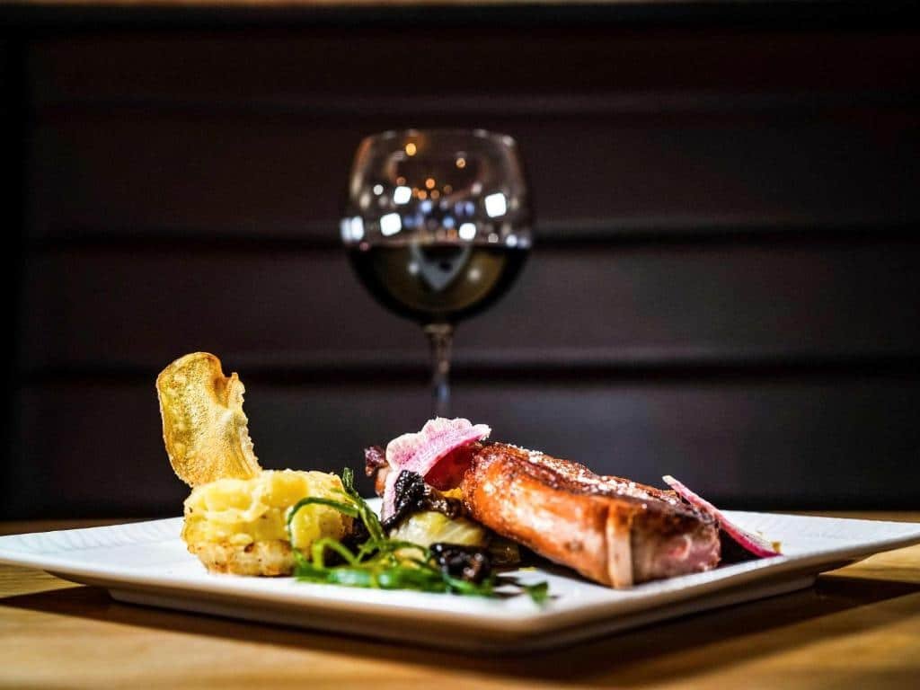 Foto de um prato cozinhado profissionalmente no Novotel Luxemburgo Centre, e uma taça de vinho acompanha atrás. 