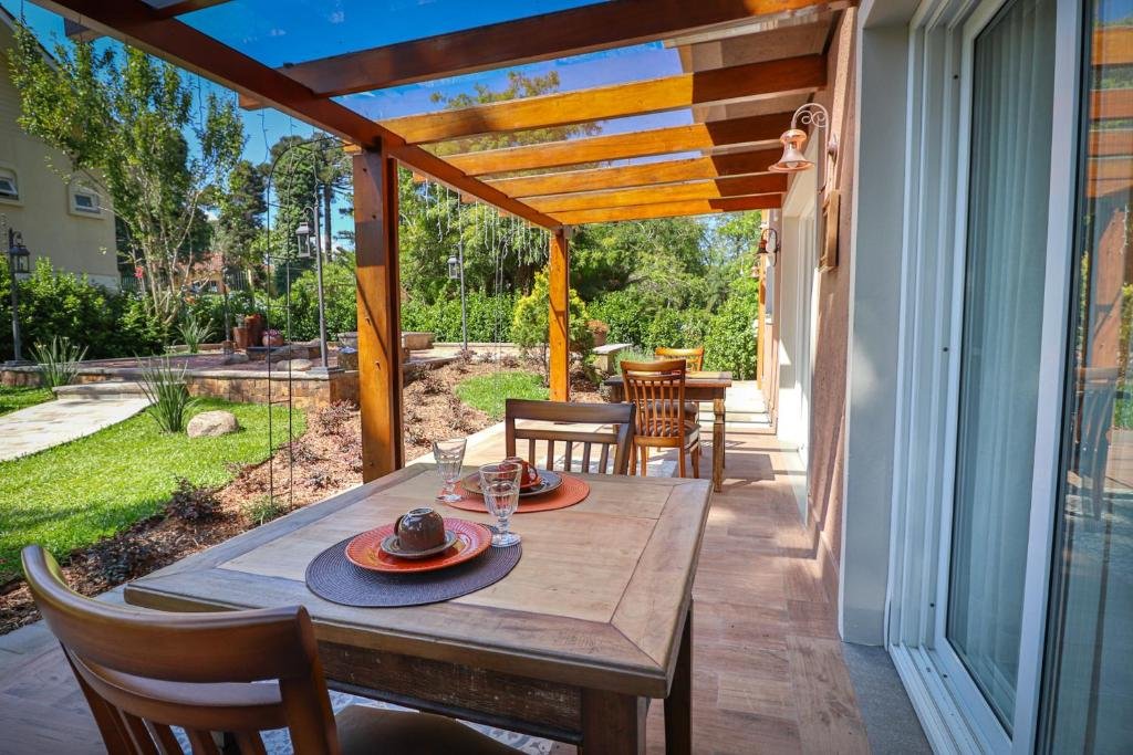 área externa do refeitório com vista para o jardim. Há duas mesas quadradas de madeiras com duas cadeiras em cada uma.