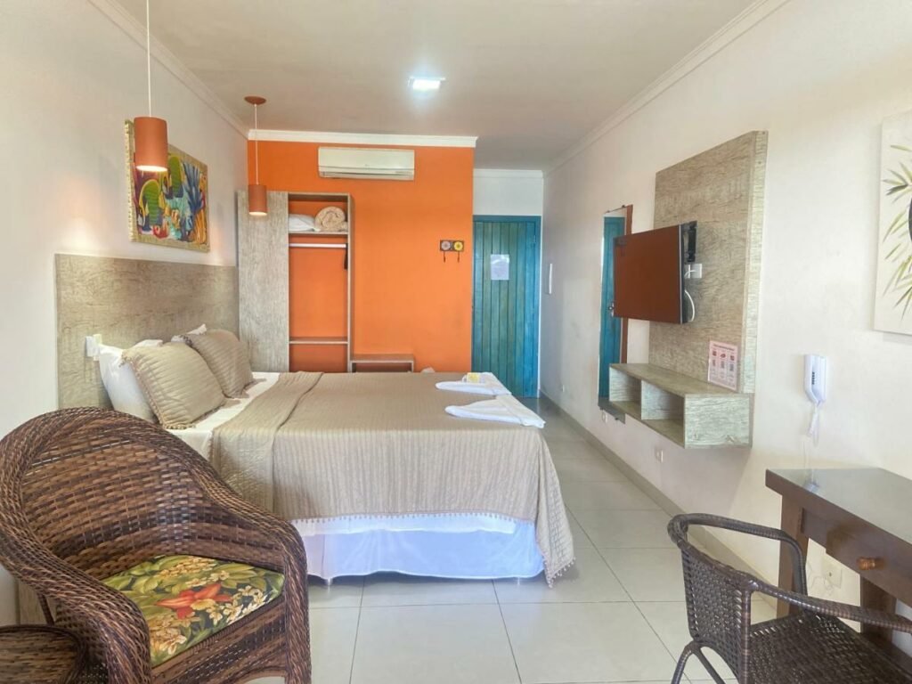 Quarto com cama de casal, armário, ar-condicionado, TV e poltrona na Pousada Kaliman