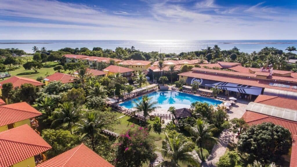 Vista aérea do La Torre Resort All Inclusive com prédios com telhados vermelhos, uma piscina, vegetação exuberante e um oceano ao fundo.