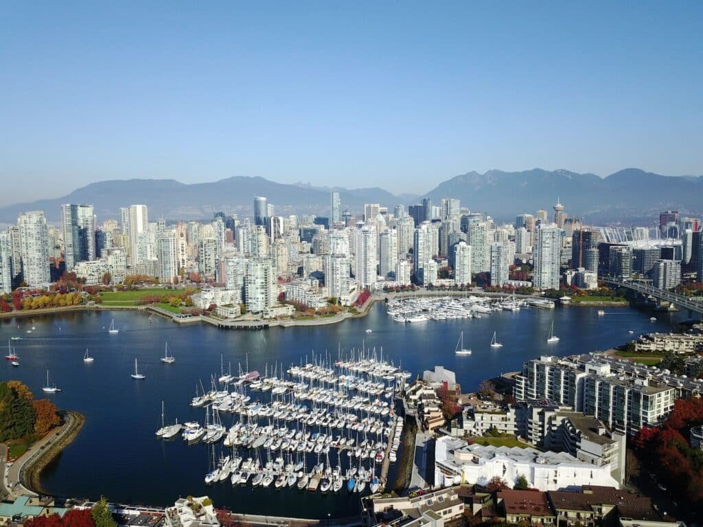 Uma foto aérea da 6th Ave em Vancouver, onde é possível ver uma extensa baía com muitos barcos estacionados e, do outro lado da baía, está a cidade 