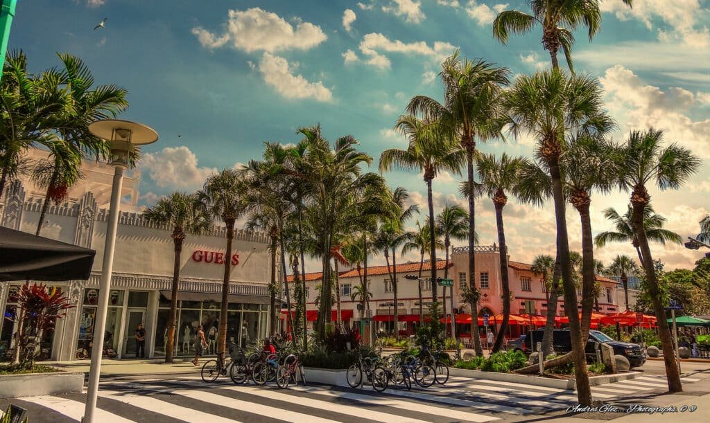 Um pedaço de Lincoln Road onde está a loja Guess, uma faixa de pedestres e um espaço para bicicletas. Várias árvores decoram o ambiente. A foto está na lista de o que fazer em Miami.