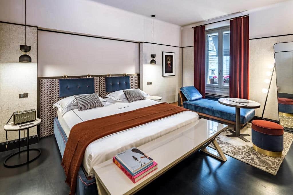 Quarto do Locanda Pandenus Brera com uma cama de casal, uma janela com cortinas, um banco no pé da cama com alguns livros, há um sofá-cama e um espelho de corpo inteiro no espaço