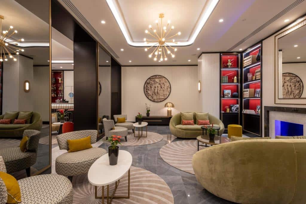 lounge do H10 Palazzo Galla com poltronas largas, mesinhas ovais e nichos com decoração nas paredes, há um lustre e o ambiente todo é bem iluminado, um painel ao estilo clássico bem trabalhado está no centro da parede