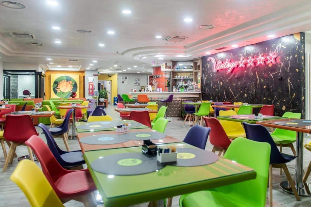 lounge do ibis Styles Roma Vintage com várias mesas e cadeiras coloridas em um tom de neon claro de verde, amarelo e rosa, sendo um dos hotéis Ibis em Roma