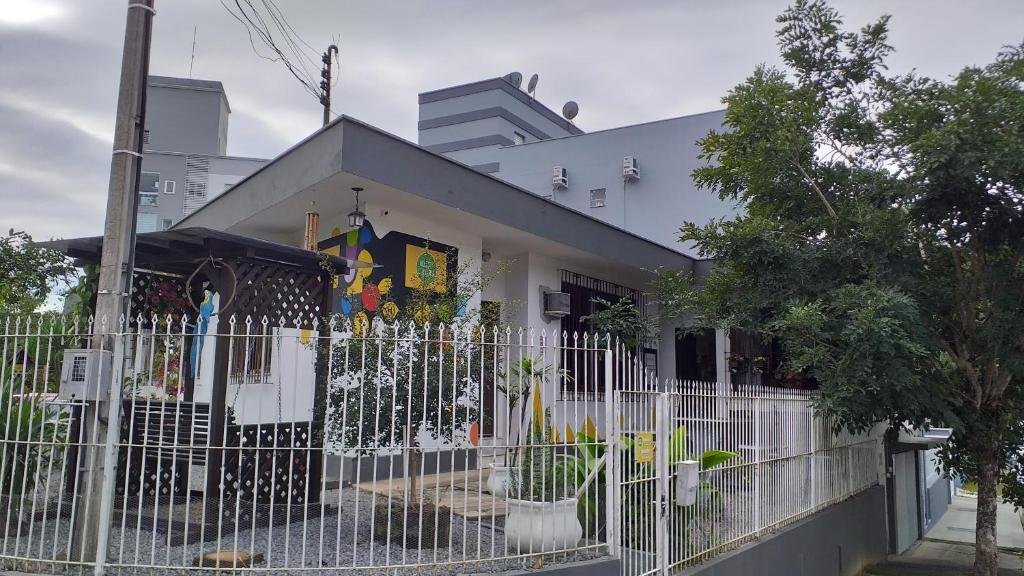 Esquina do Hostel Lumaria, com grades brancas certando a casa, que também tem diferentes tipos de flores decorando o lugar