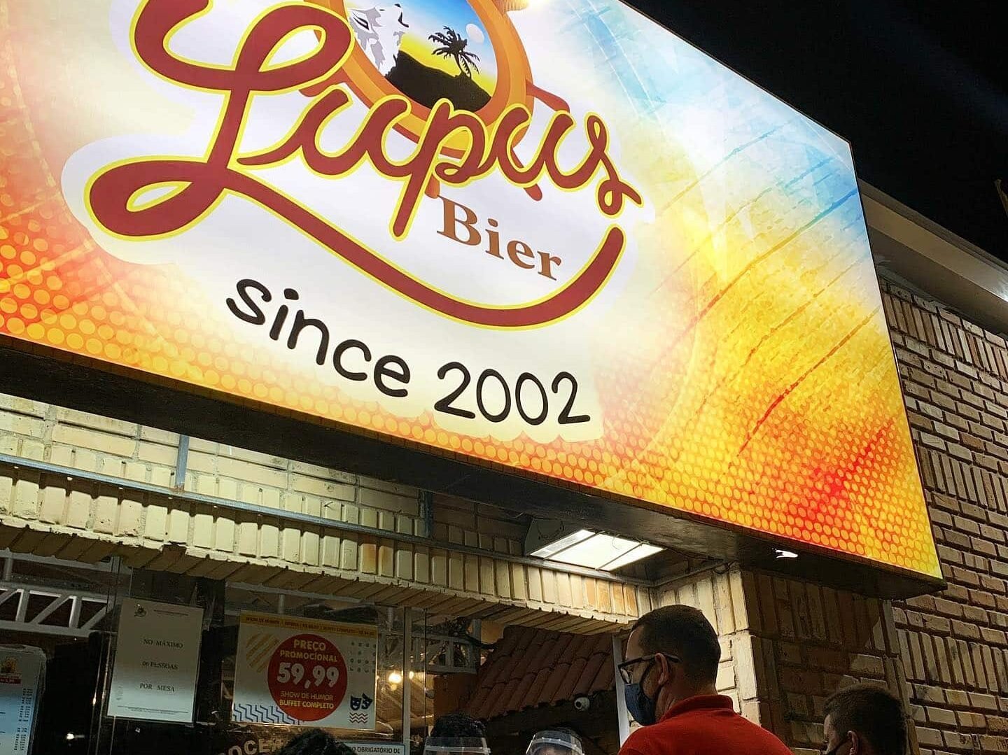 Fachada do Lupus Bier, um bar em Fortaleza. O outdoor é em cores quentes e contém o nome do estabelecimento. A foto foi tirada à noite, e foca apenas no letreiro, no entanto, é possível ver parte da entrada do prédio ao redor.