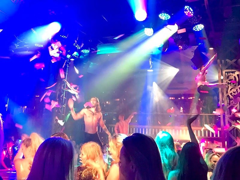 Dançarinos sem camisa durante uma perfomance do Magic Mike. O local é iluminado com luzes coloridas. A multidão dança e balança os braços. Foto para ilustrar o post shows em Las Vegas.