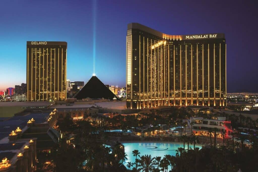 Fachada do Mandalay Bay um prédio preto com iluminação dourado, ao redor há piscinas e as atrações turísticas como pirâmides 