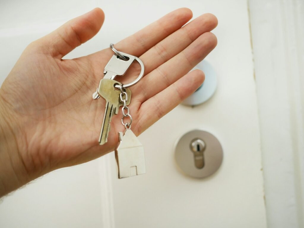 Mão branca com uma chave e ao fundo tem as fechaduras de uma porta