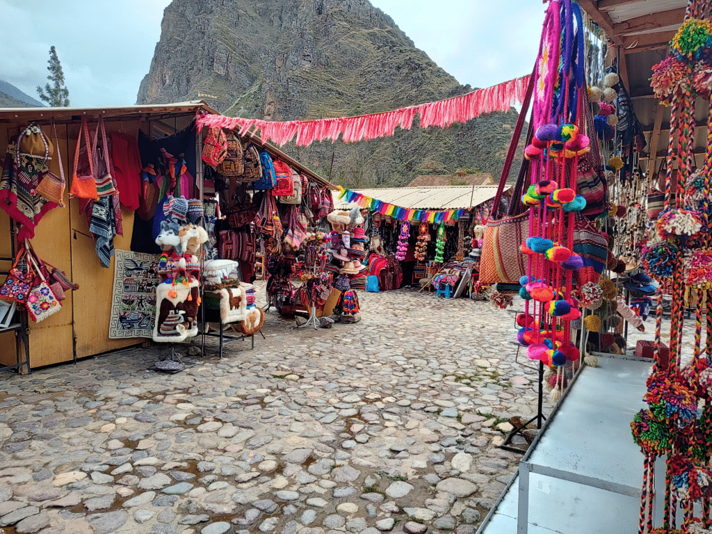 Mercado de Ollantaytambo, com várias lojinhas coloridas, com diversos produtos artesanais sobre uma rua de pedra.