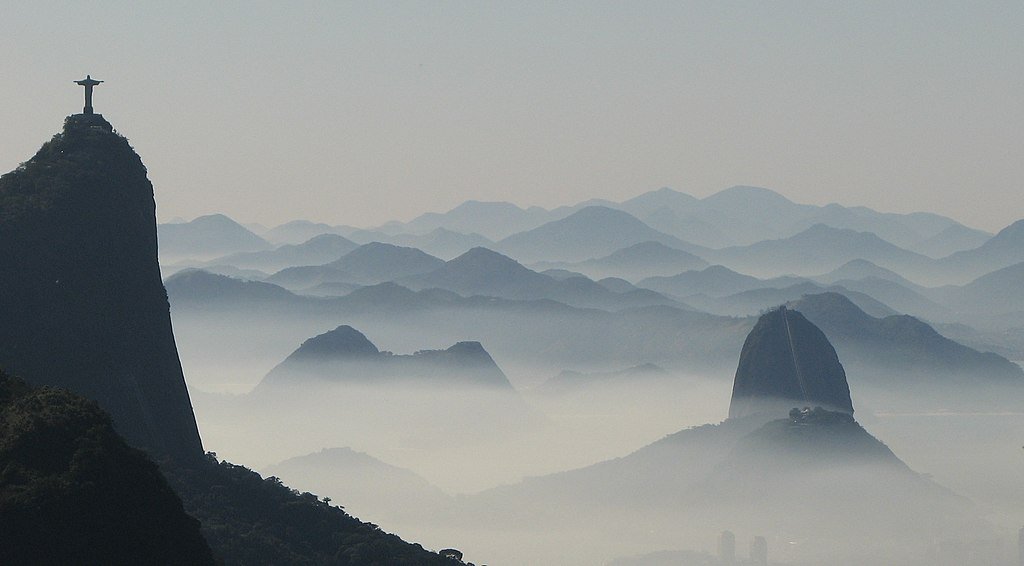 Vista distante da paisagem enevoada do Rio de Janeiro, com a estátua do Cristo Redentor e o Pão de Açúcar. Essa é a paisagem de uma das trilhas no Rio de Janeiro.