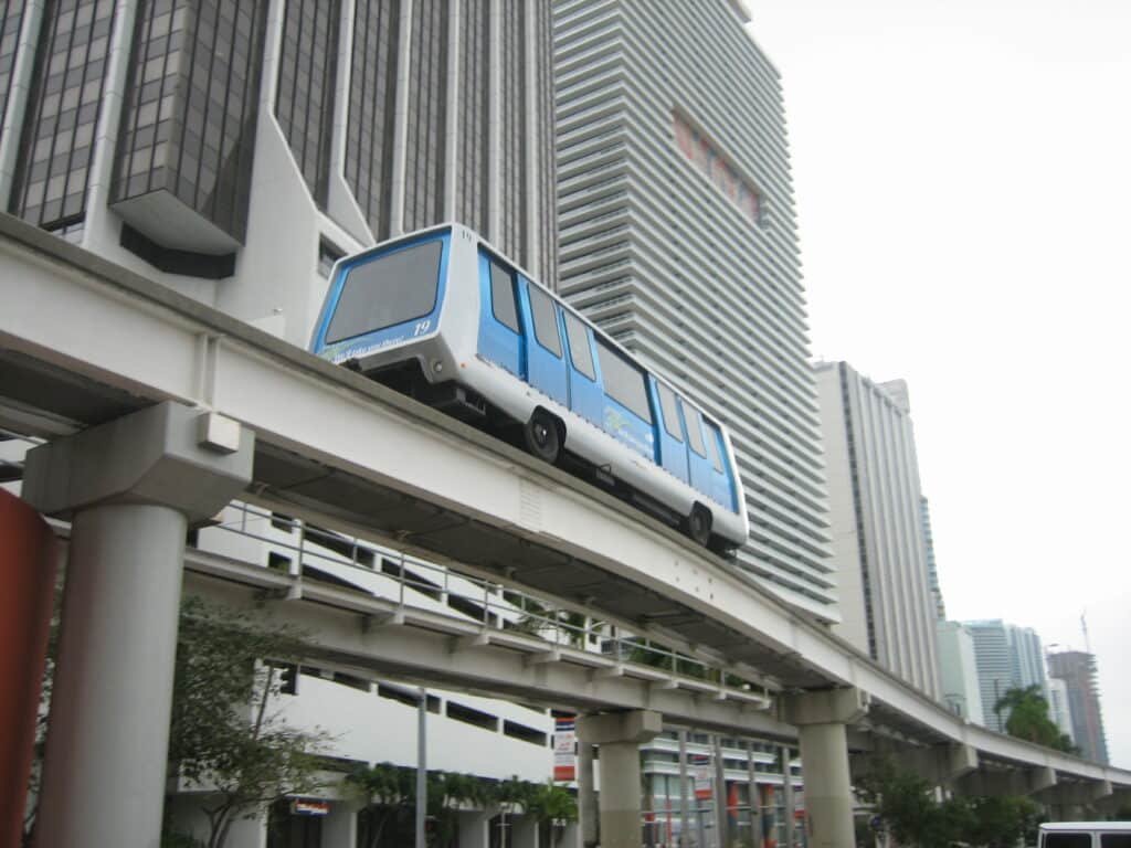 Metromover andando nos trilhos acima das ruas. Ao lado dele estão vários prédios.