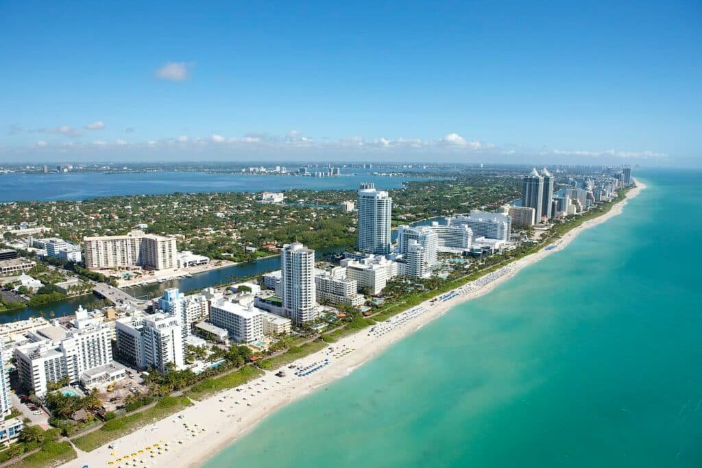 Visão geral das praias de Miami. O mar está do lado direito e, do lado esquerdo, estão os diversos prédios, ruas e vegetação.