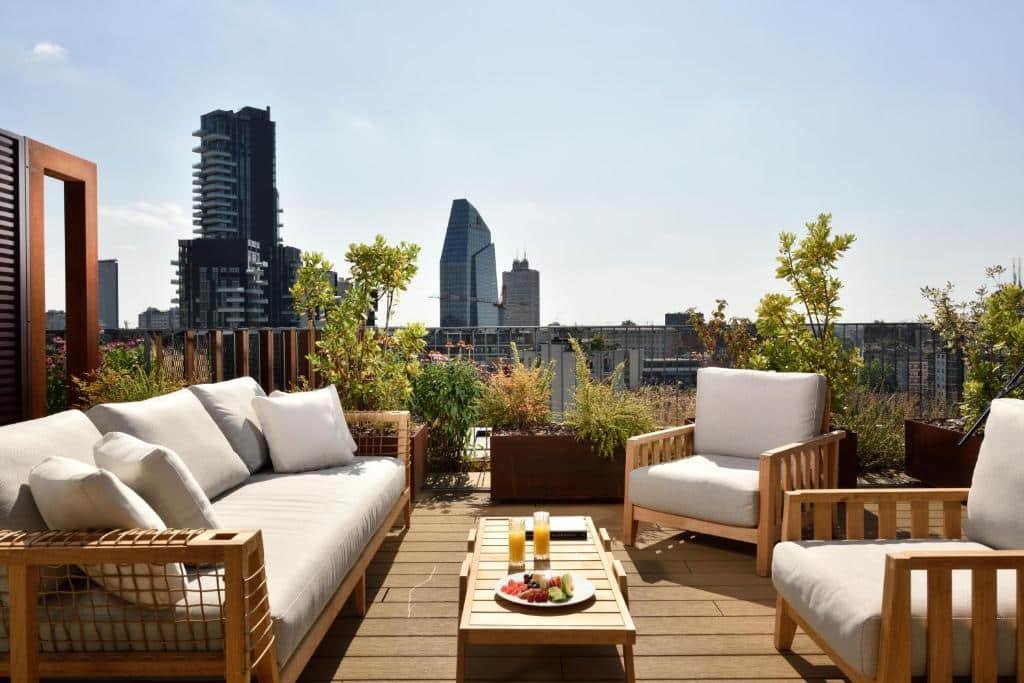 Terraço na cobertura do Milano Verticale | UNA Esperienze com poltronas e um sofá estofados com vista para a cidade, há vasos de plantas e uma pequena mesinha no centro, para representar os melhores hotéis em Milão