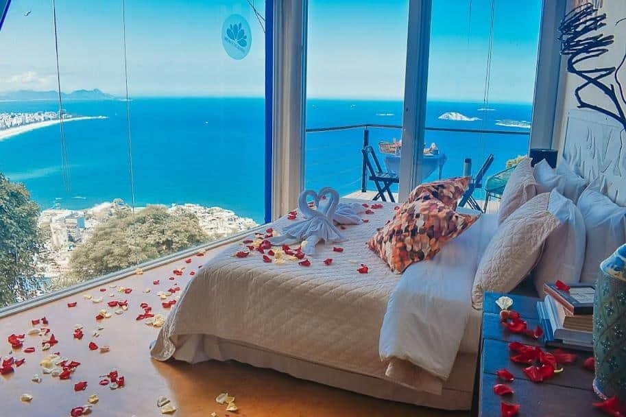 Quarto com janelas grandes com vista para o litoral. A cama é adornada com pétalas de rosas e cisnes de toalha, levando a uma sacada para representar um dos melhores lugares para lua de mel