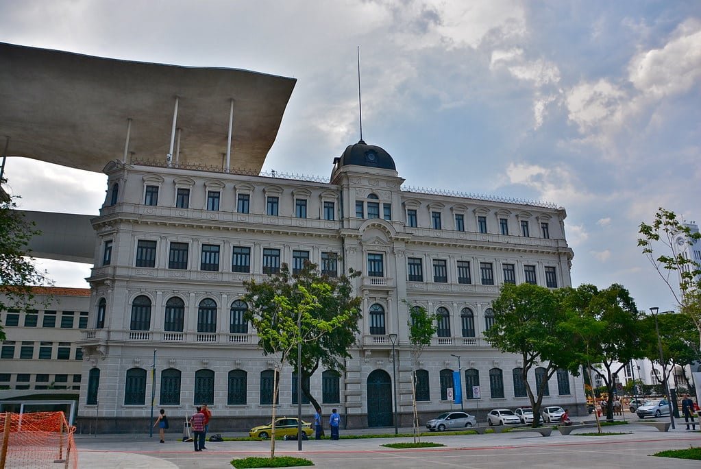 Museu de Arte do Rio com vários andares e uma cúpula central, cercado por árvores e algumas pessoas na calçada. Imagem para ilustrar o post sobre museus no Rio de Janeiro.