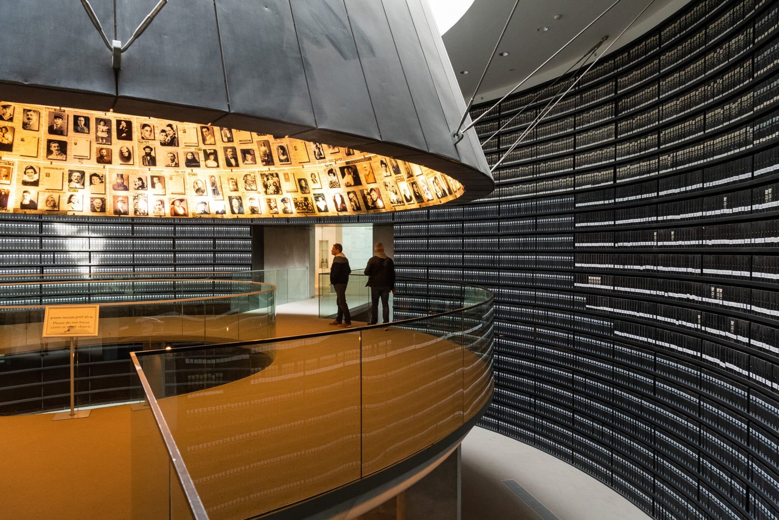 Duas pessoas em pé em uma passarela circular em um museu. Paredes exibem inúmeras fotografias e prateleiras com fichários etiquetados.