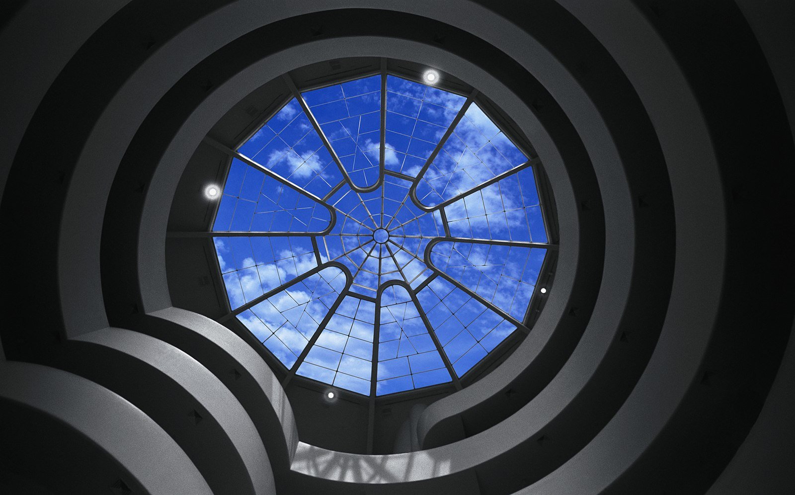 Vista do Museu Solomon R. Guggenheim olhando para uma claraboia circular com um padrão de grade, revelando um céu azul com nuvens dispersas.