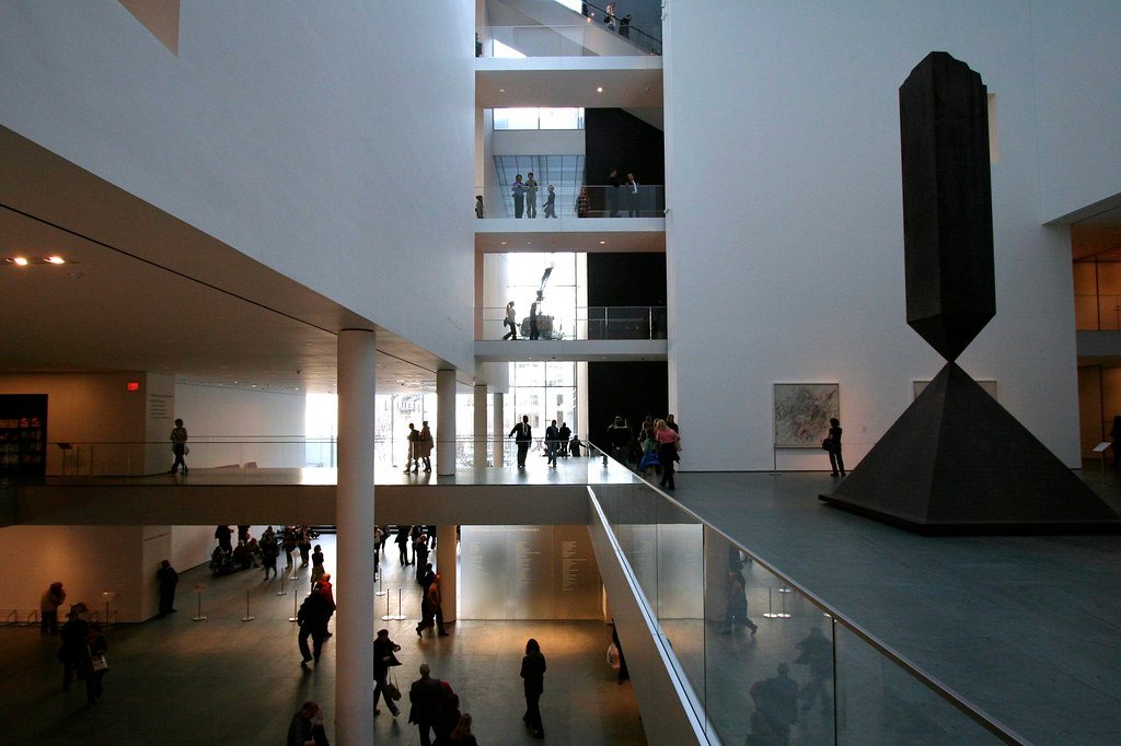 O interior do MoMa - Museum of Modern Art com vários andares, pessoas caminhando e uma grande escultura geométrica exposta no lado direito.