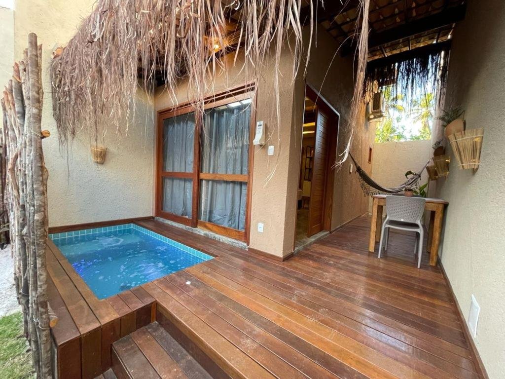 Área externa do Naim Milagres, com piscina/hidro privativa, sacada de vidro fechada e com cortinas à frante, além de mesinha com cadeiras e rede de descanso ao fundo