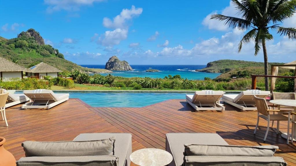 Deck da piscina do Nannai Solar dos Ventos, uma das dicas de pousadas em Fernando de Noronha, com vista para o mar da ilha e para uma formação rochosa no oceano