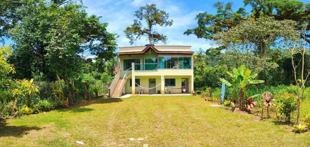 Frente do Pacífico Sul Suítes. Uma casa com primeiro andar e varanda, um jardim na frente e mata dos dois lados.