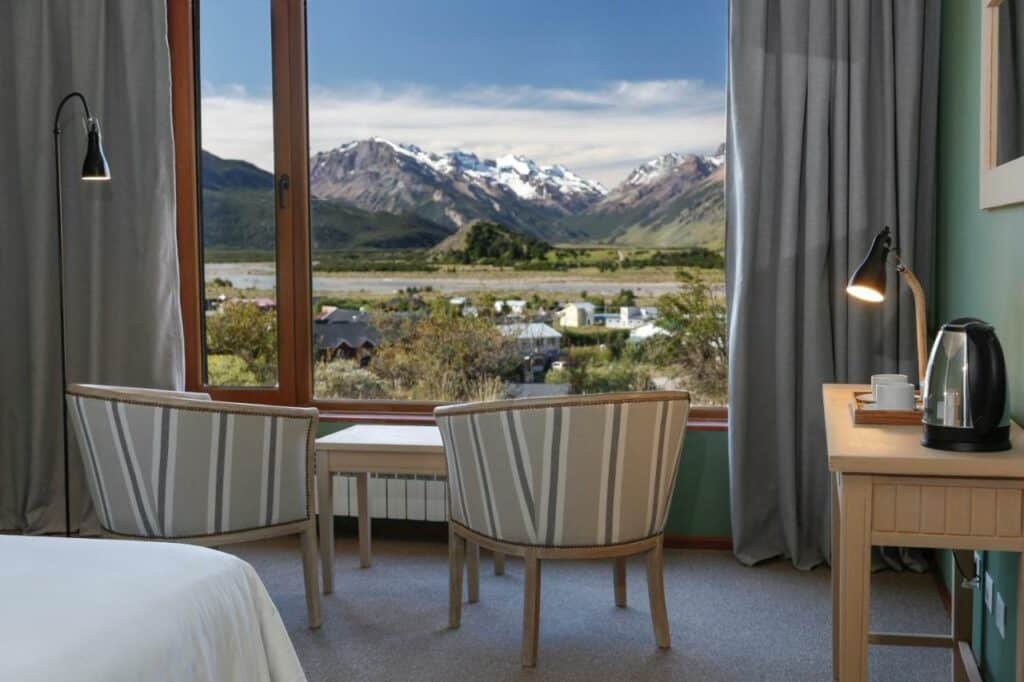 Imagem do quarto Los Cerros del Chaltén Boutique Hotel com duas cadeiras a frente com vista para a janela panorâmica com vista para as montanhas.