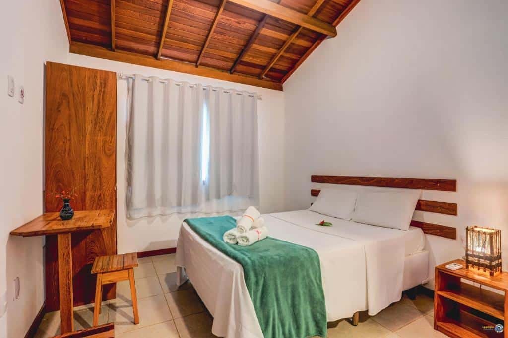 Quarto no Paradiso Flat Itacaré. Há uma cama box de casal à direita, e na sua frente há uma mesa com um banco e um guarda-roupa. A janela está ano fundo, ao lado a cama. Representa o post sobre airbnb em Itacaré.