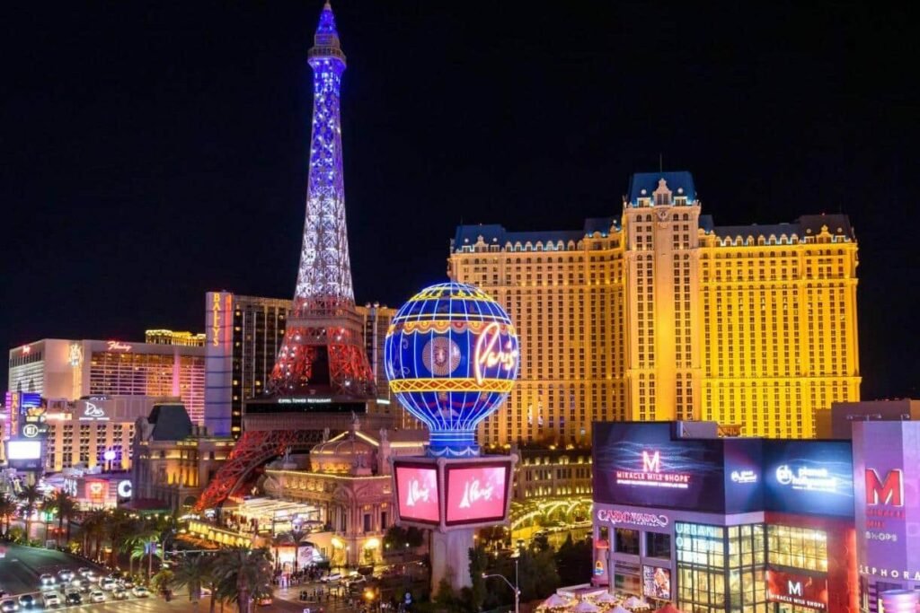 Vista de longe da torre eiffel do hotel Paris Las Vegas. Ela está toda iluminada, assim como os prédios e uma réplica do Le Géant, um balão de ar quente. Ele fica quase ao lado da torre. Foto para o post de pontos turísticos em Las Vegas.