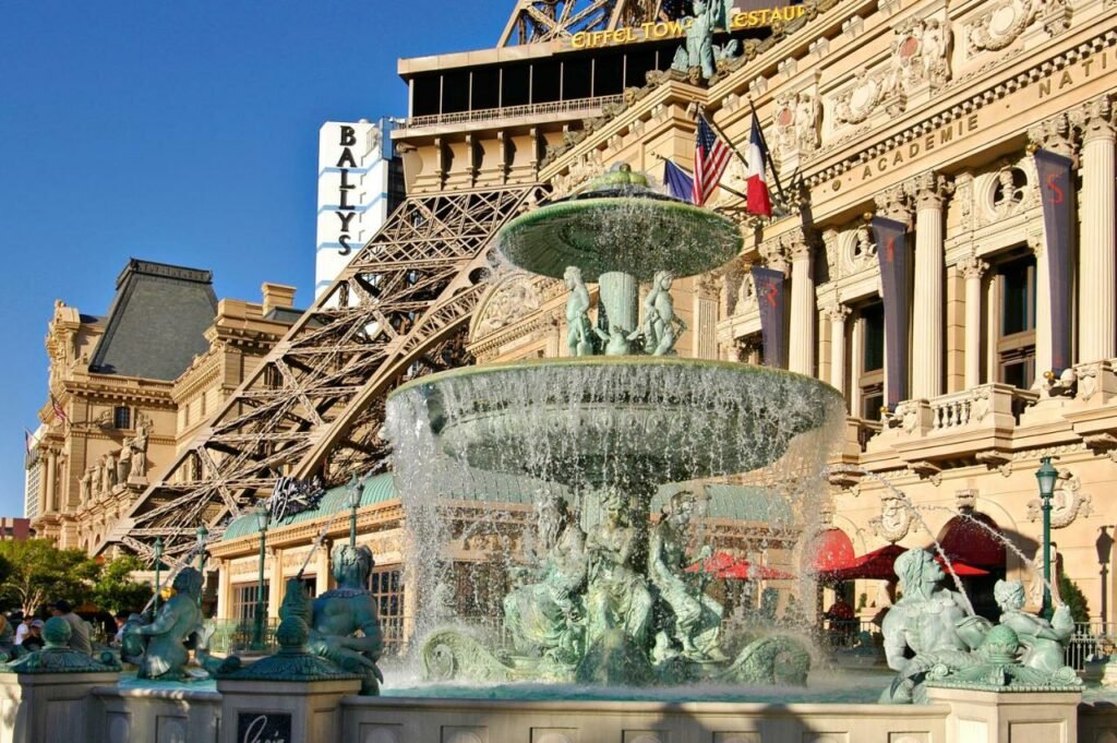 Fonte de água com diversas esculturas, parecendo de Paris, na parte exterior do Paris Las Vegas, ao lado da base da torre.