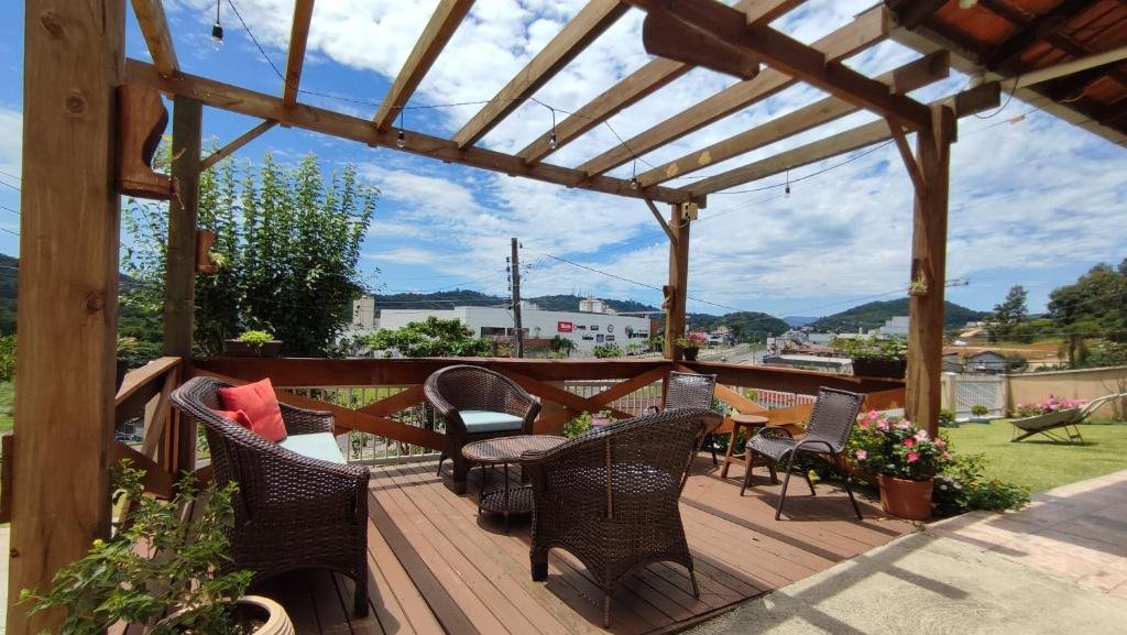 Deck de madeira da Park House Pousada, com poltronas e cadeiras espalhadas e uma vista ao fundo dos prédios da cidade e montanhas. Ao ado, há um gramado com flores rosas e folhas verdes