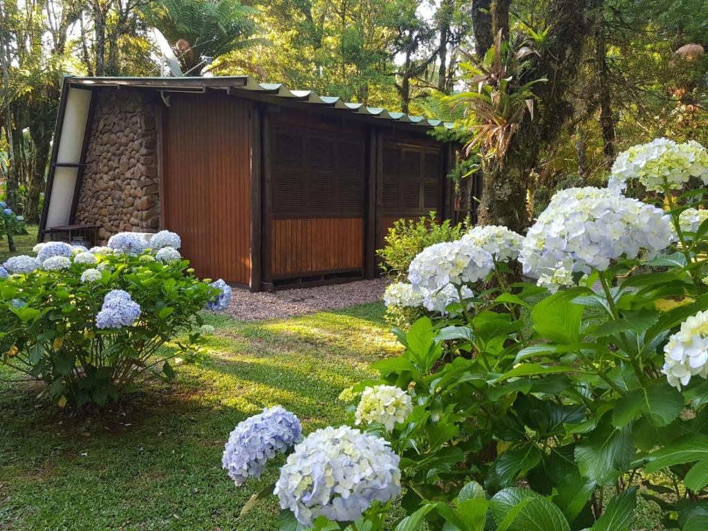 Exterior do Parque do SESI Canela. Há um chalé de madeiro em meio à um jardim com gramado baixo, árvores e várias flores