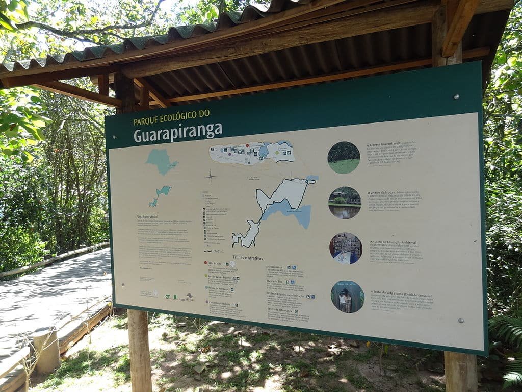 Placa no Parque Ecológico do Guarapiranga, exibindo um mapa detalhado do parque, informações e fotos sob um teto de madeira.