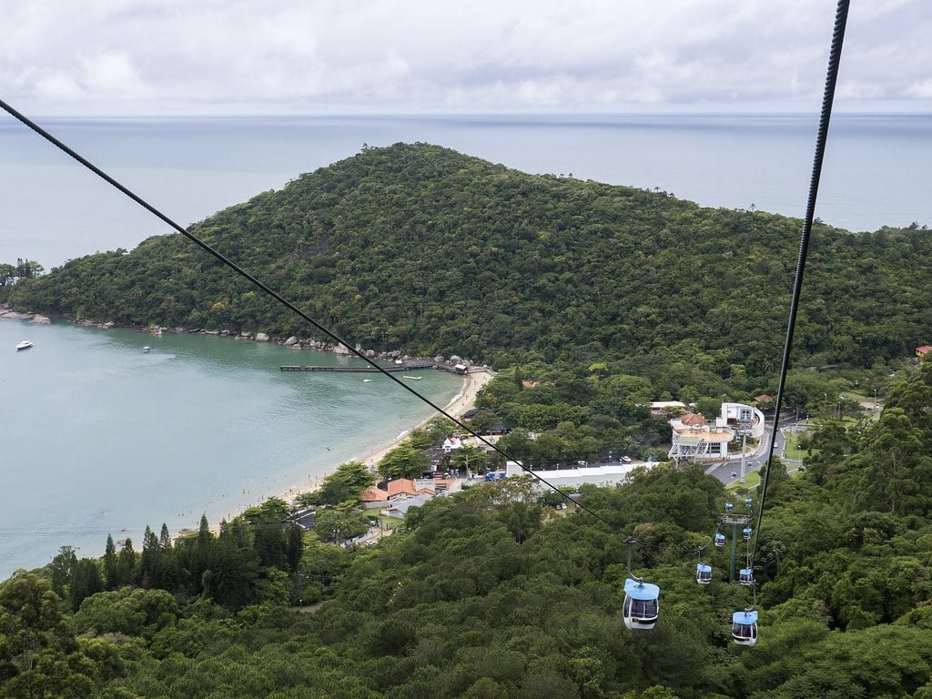 Vista do bondinho do Parque Unipraias. Vários. Do lado direito váriosbondinhos com vista das árvores, do lado esquerdo o mar. Imagem para ilustrar post sobre o que fazer em Balneário Camboriú.