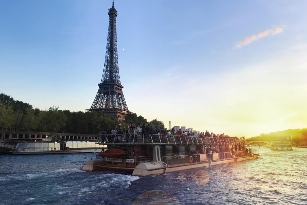 Um barco cheio de pessoas navega em um rio com a Torre Eiffel ao fundo durante o pôr do sol para ilustrar um dos passeios em Paris.