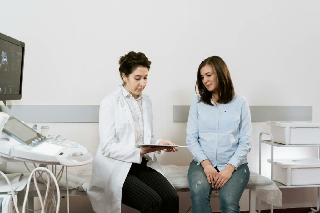 Uma médica junto de uma paciente, as duas sentadas em dentro de uma sala de consultório médico