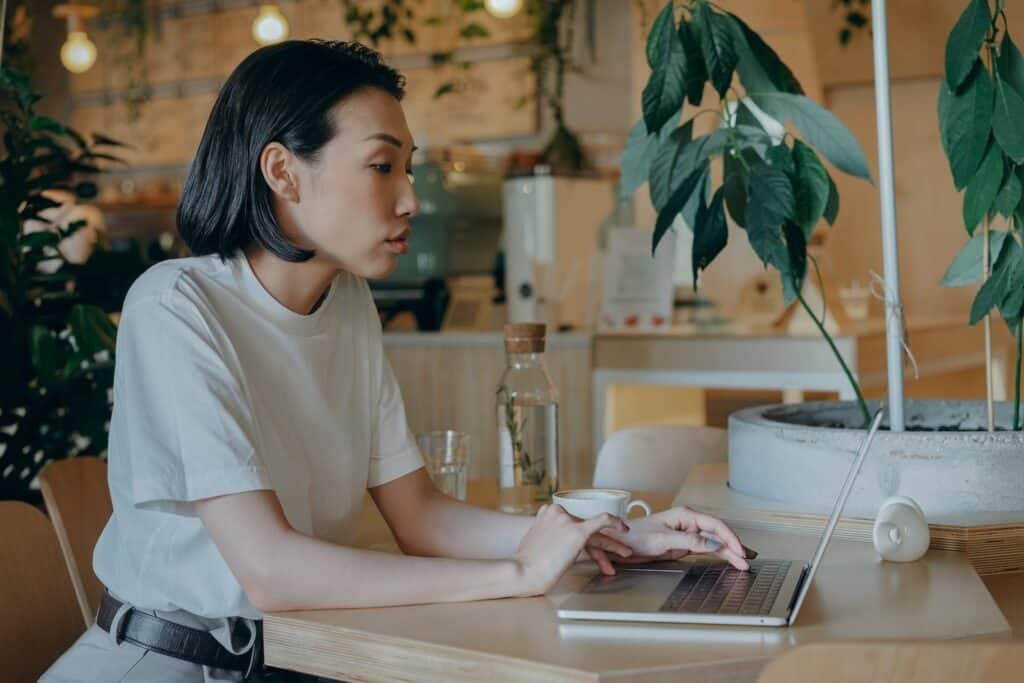 Uma mulher asiática sentada em uma mesa mexendo em um notebook