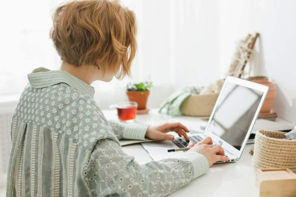 Uma mulher sentada em uma mesa usando um notebook e segurando um lápis em uma das mãos