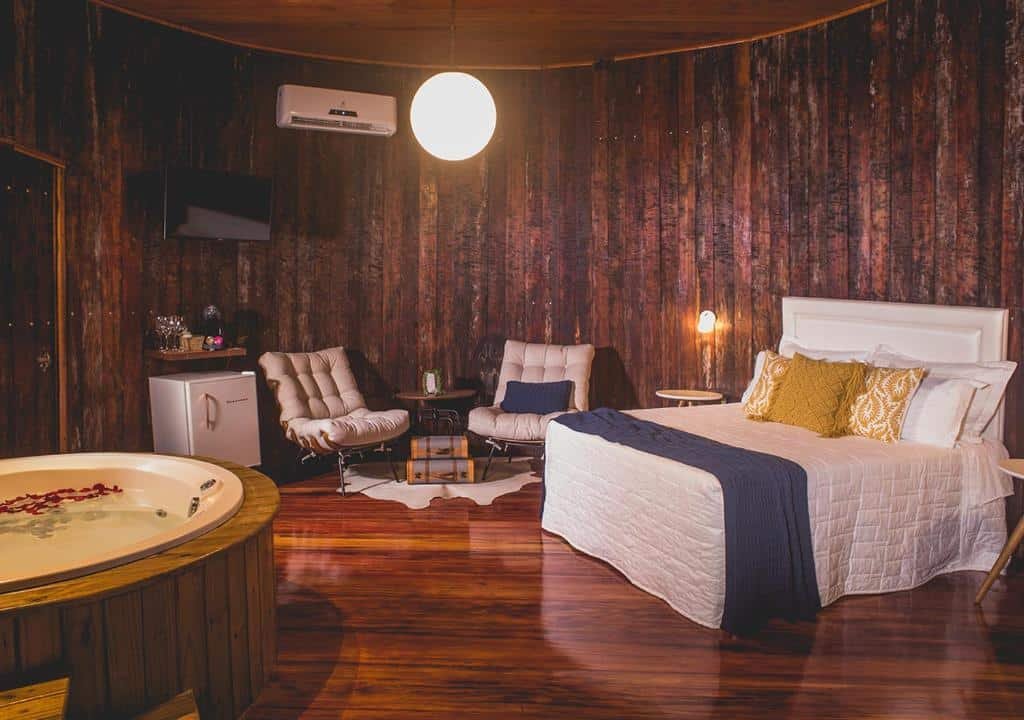 Quarto de casal do Pipas do Vale, elaborado dentro de uma estrutura que imita um tonel de vinho, com paredes arredondadas, frigobar, poltronas, cama, TV, ar-condicionado e banheira de hidro