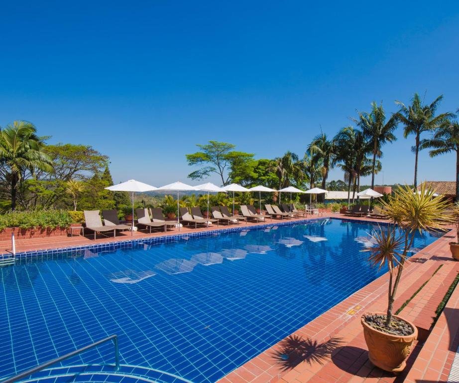 Piscina ao ar livre do Hotel Villa Rossa, uma das opções de hotéis fazenda em São Paulo, com azulejos azuis, cercada por espreguiçadeiras, guarda-sóis e palmeiras.