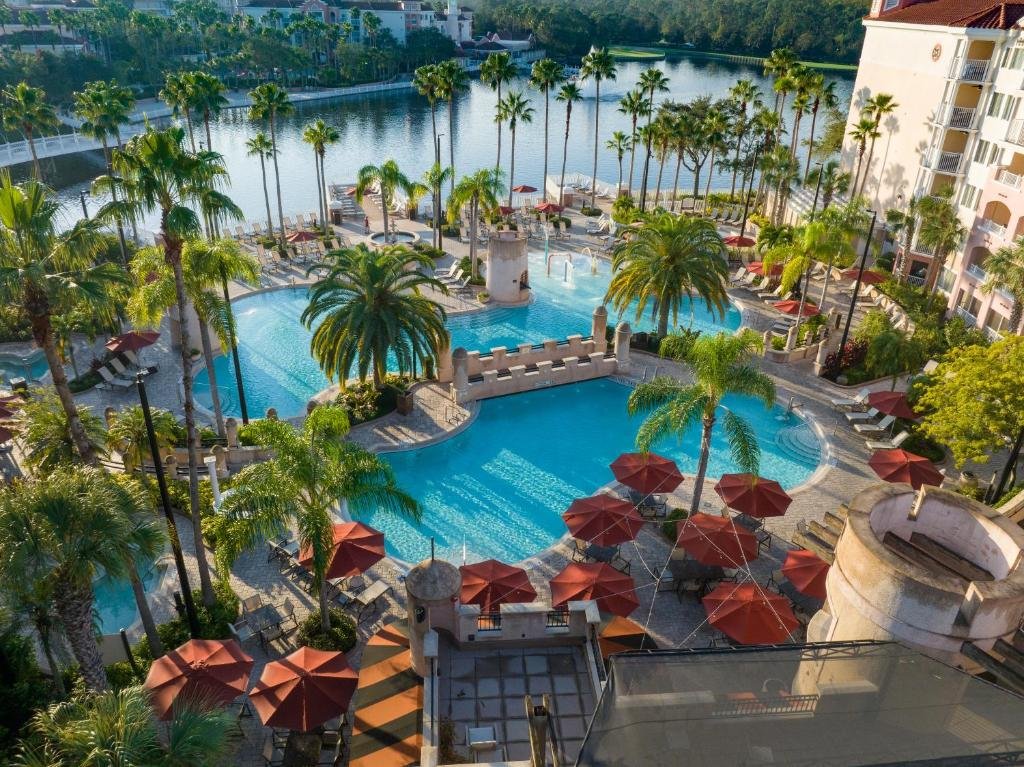 piscina grande e redonda com uma ponte conectando as duas partes, com várias palmeiras ao redor, além de mesinhas e caderias do Marriott