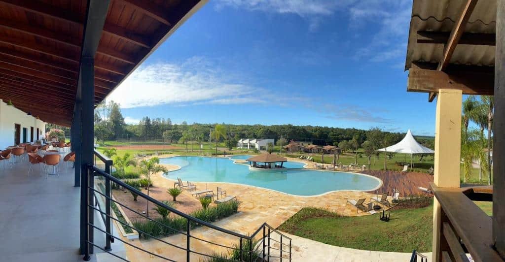 Uma área de piscina do Vale Das Águas Fazenda Resort, um dos hotéis fazenda em São Paulo, com muito verde ao redor, assentos ao ar livre e um céu azul ao fundo.