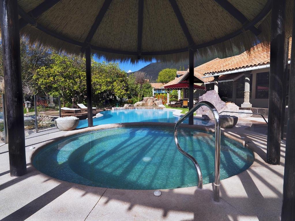 área aberta da piscina do Aranwa Sacred Valley Hotel & Wellness com duas piscinas arredondadas, uma coberta e outra não. Há várias árvores e vegetação natural ao redor das piscinas.